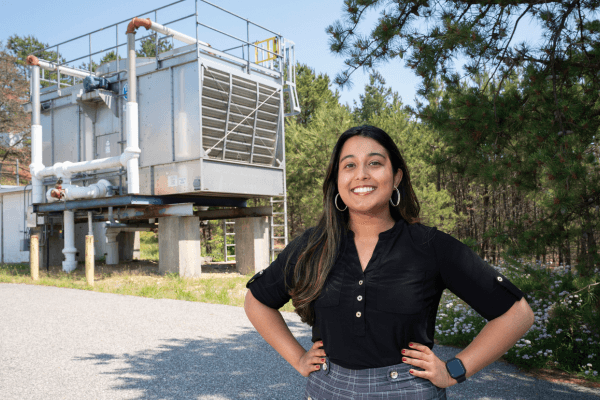 Brookhaven Lab engineer Thea Vijaya Kumar in front of a cooling tower adjacent to the ring of the Relativistic Heavy Ion Collider (RHIC).