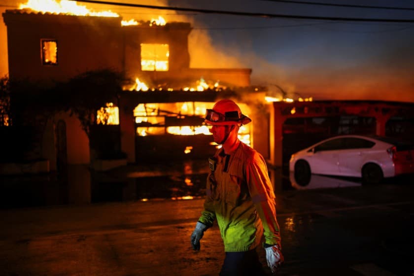 A firefighter walks next to a burning home, as powerful winds fueling devastating wildfires in the Los Angeles area force people to evacuate, in Malibu, California, U.S. January 8, 2025. REUTERS/Daniel Cole