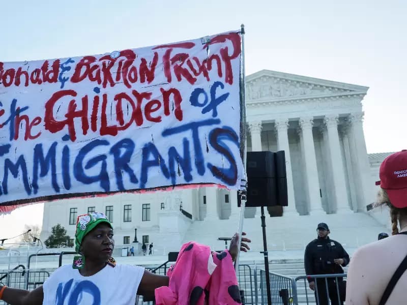 A demonstrator holds a sign as another wears a cap reading, "Immigrants make America great" outside the U.S. Supreme Court building on the day the court is expected to hear oral arguments on the legality of the Trump administration's effort to limit birthright citizenship for the children of immigrants, in Washington, D.C., U.S., April 1, 2026. 