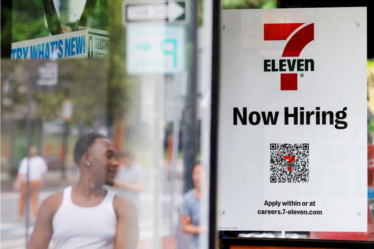 A 7-Eleven convenience store has a sign in the window reading 'Now Hiring' in Cambridge, Massachusetts.
