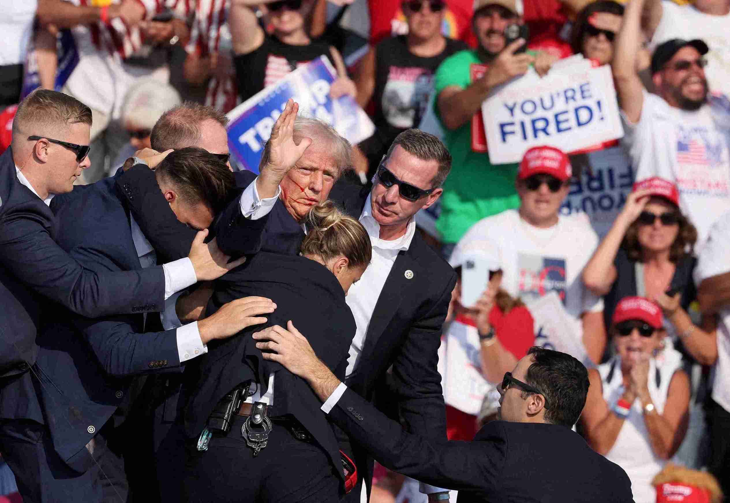 Trump gestures with a bloodied face while he is assisted by U.S. Secret Service personnel after he was shot in the right ear during a campaign rally at the Butler Farm Show in Butler.