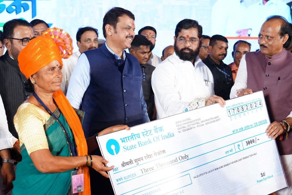 Maharashtra Chief Minister Eknath Shinde accompanied by his deputies Devendra Fadnavis and Ajit Pawar hands a symbolic cheque to a beneficiary of a government welfare scheme, in Kinhi, Maharshtra, India Aug.24, 2024.